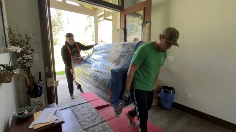 Movers carrying a protected sofa through a doorway